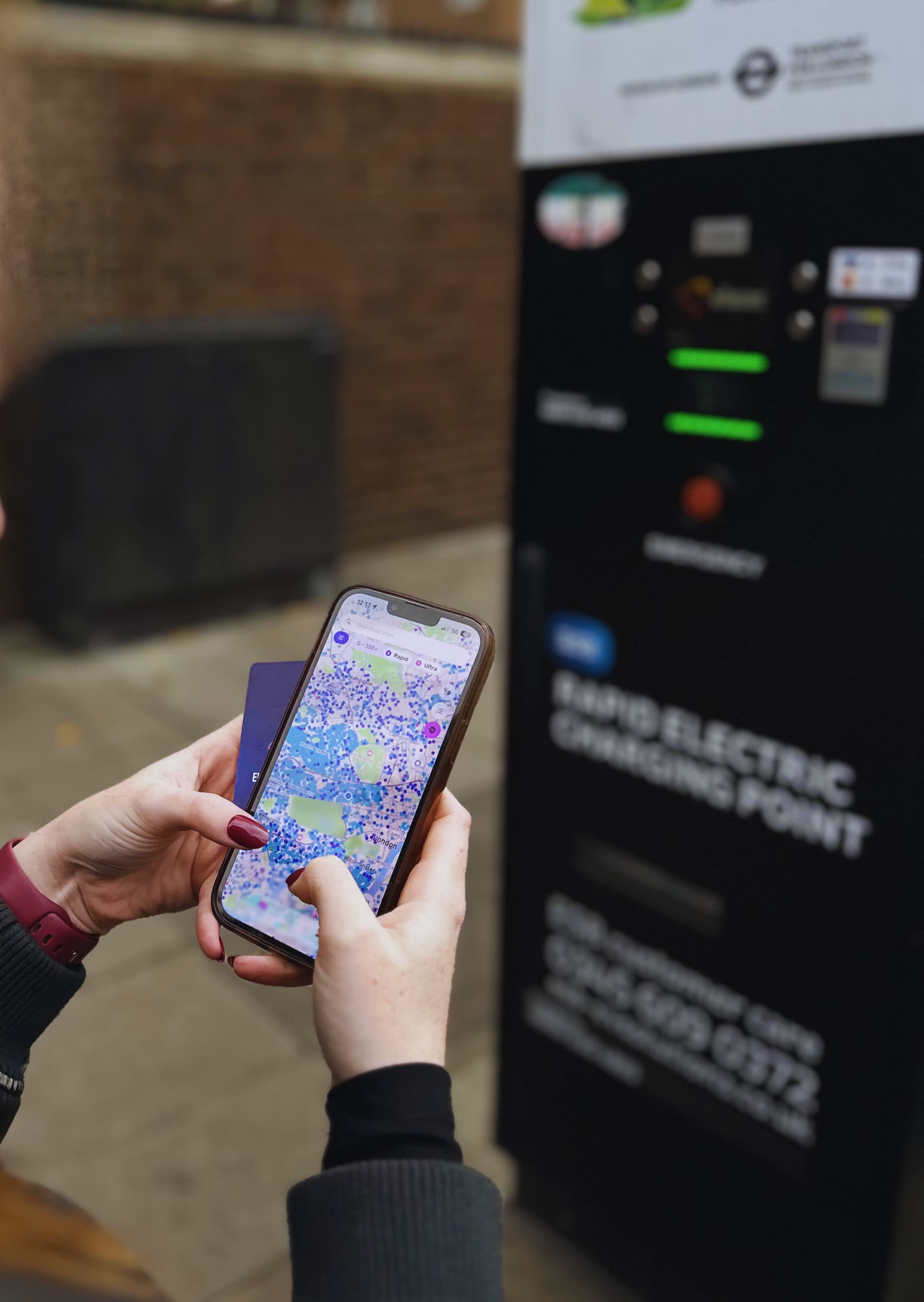 Person using a smartphone map app near an electric vehicle charging station on a city street.